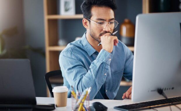 Serious, business man and thinking on computer in office, internet research and website. Focused male employee, desktop and solution of ideas, planning decision and review strategy, project or vision.